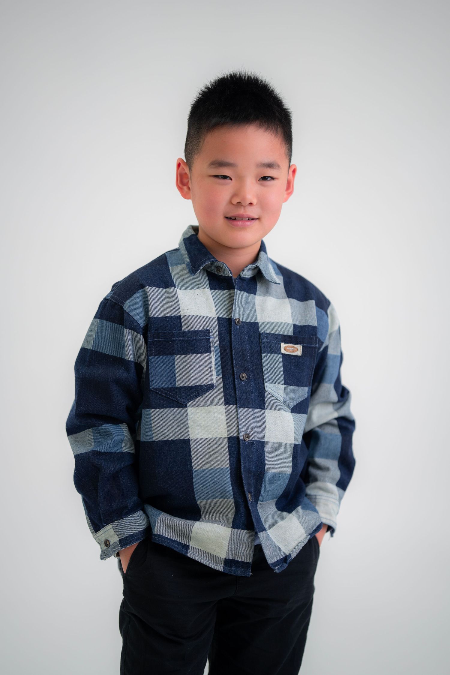 Child wearing blue plaid flannel shirt poses against white background. in Melbourne photography studio
