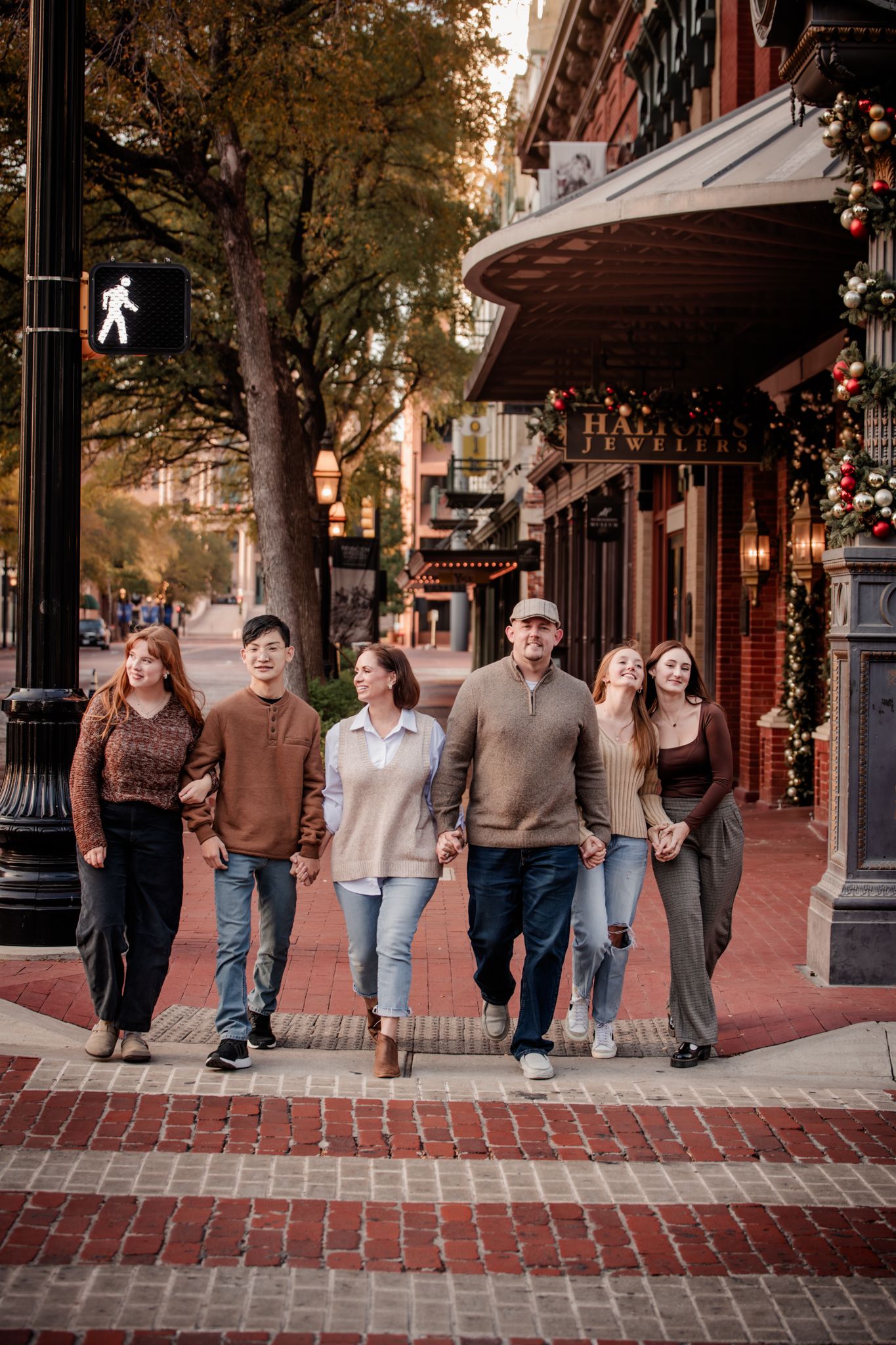 Group of people walking together along a brick sidewalk in front of storefronts at dusk.