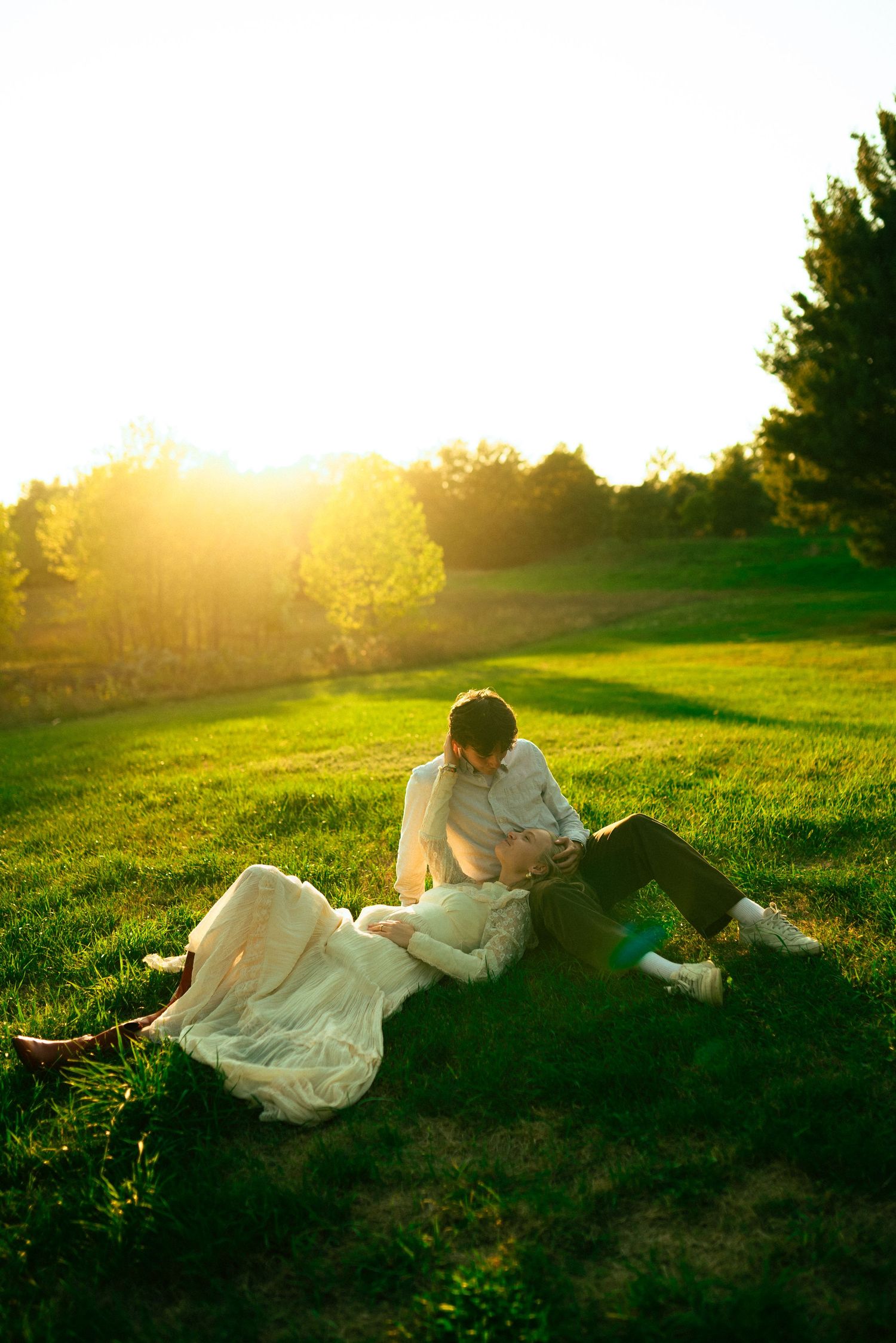 engaged couple laying in the grass at sunset