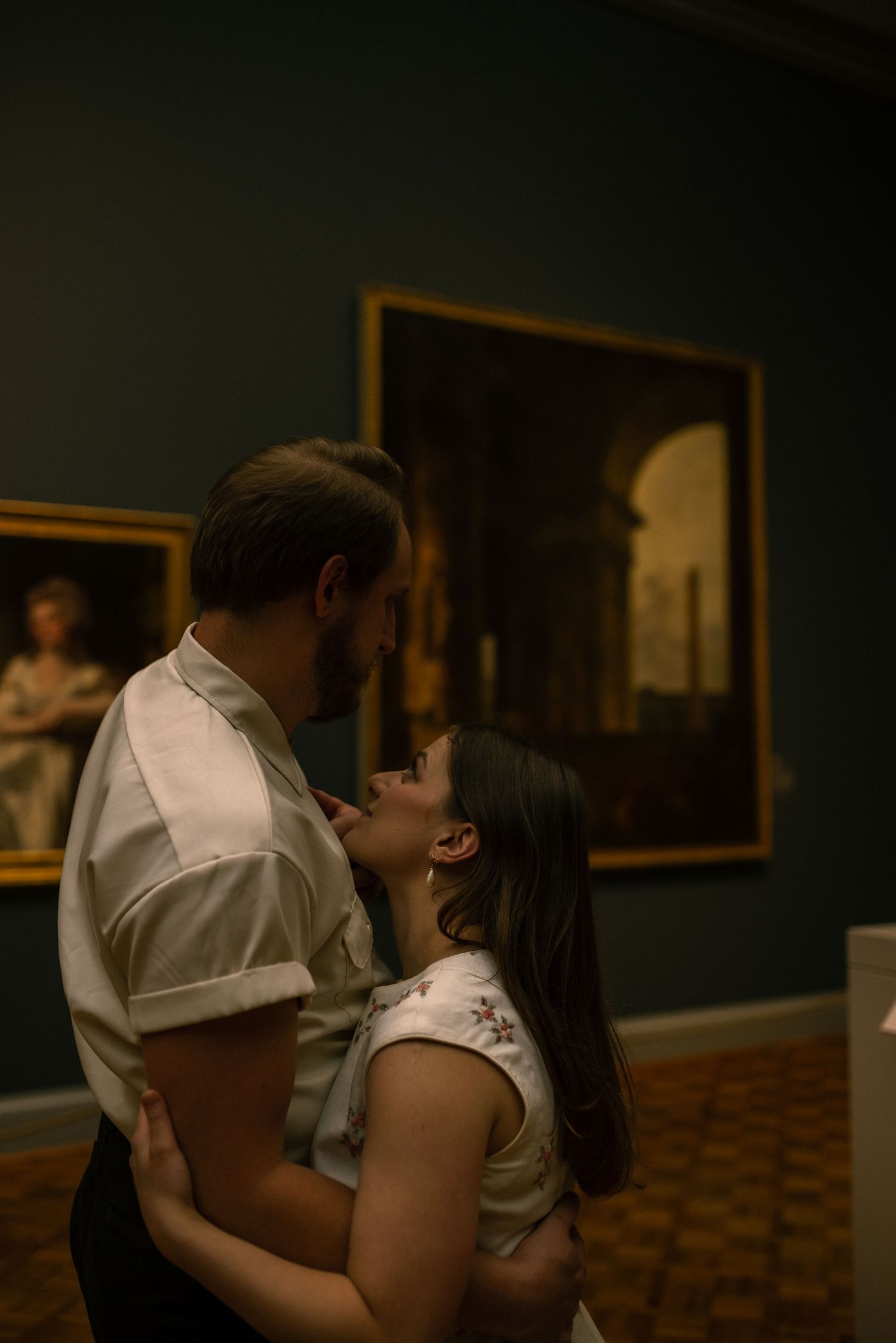 Engaged couple look at each other close while standing in an art museum