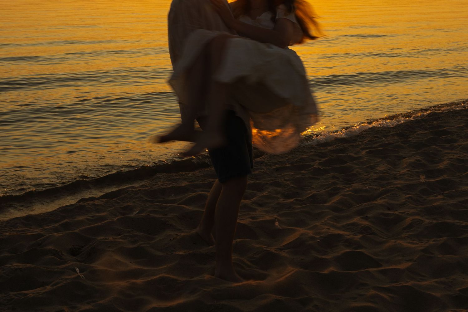 Cropped sunset beach photo of guy holding a girl and spinner her around with motion blur