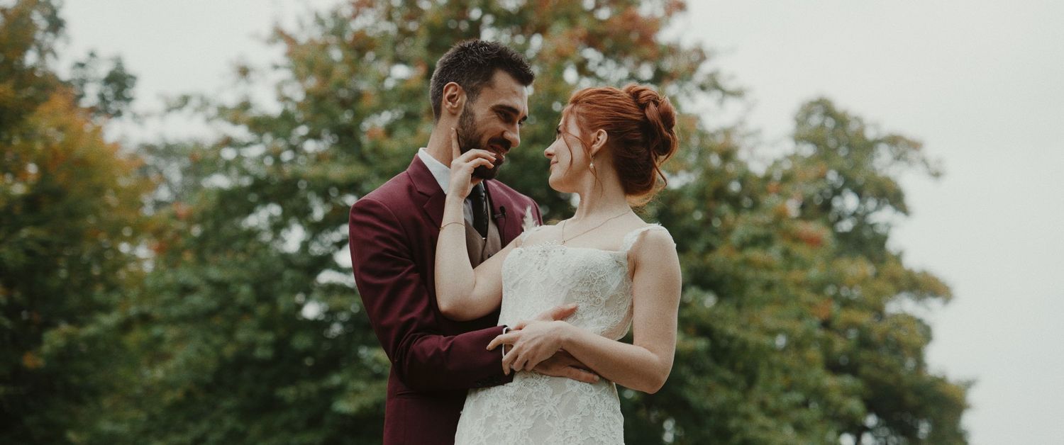 A couple shares a romantic moment outdoors during their wedding photoshoot with autumn trees in the background.