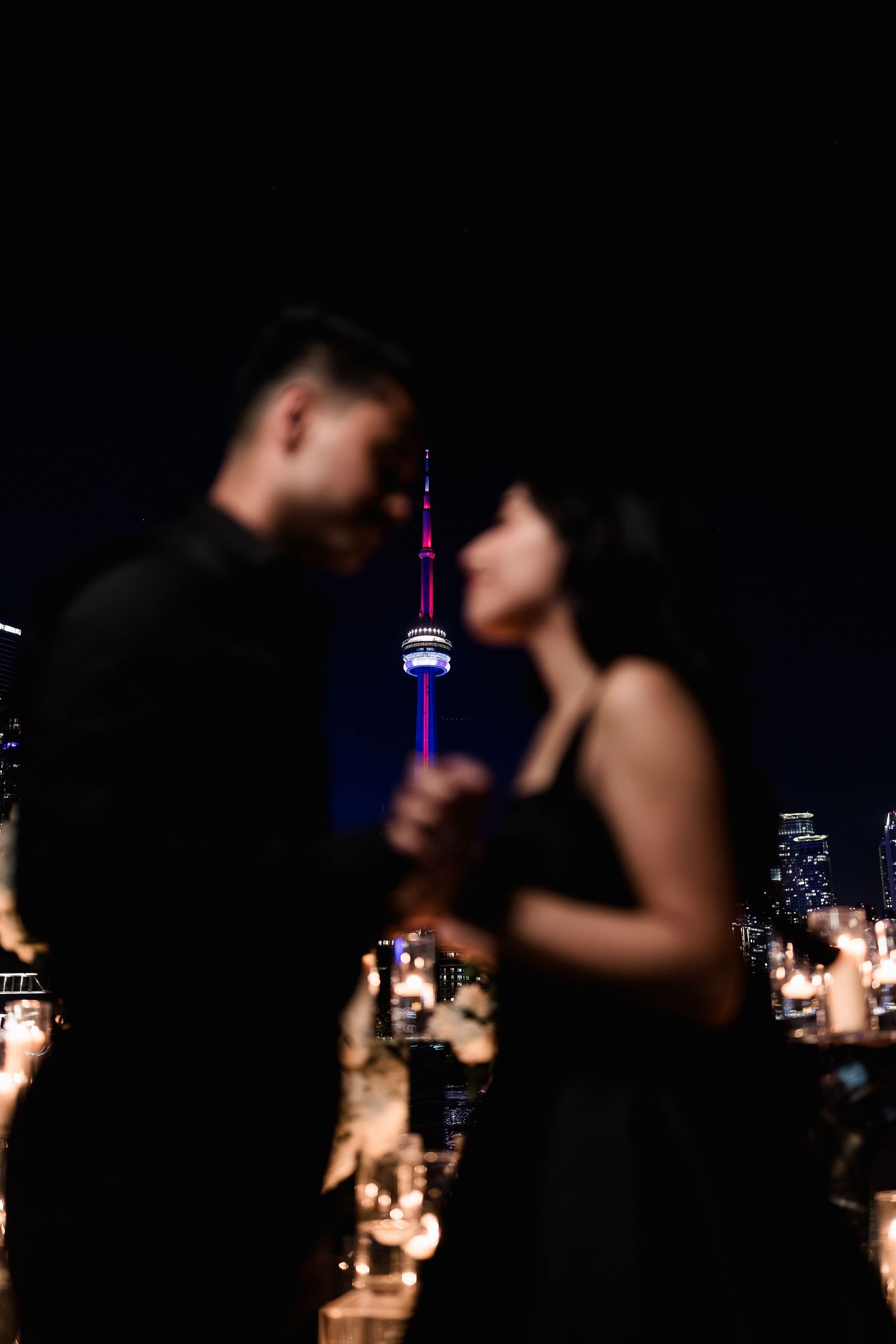Silhouetted figures against a dark city skyline with illuminated CN Tower in Toronto at night.