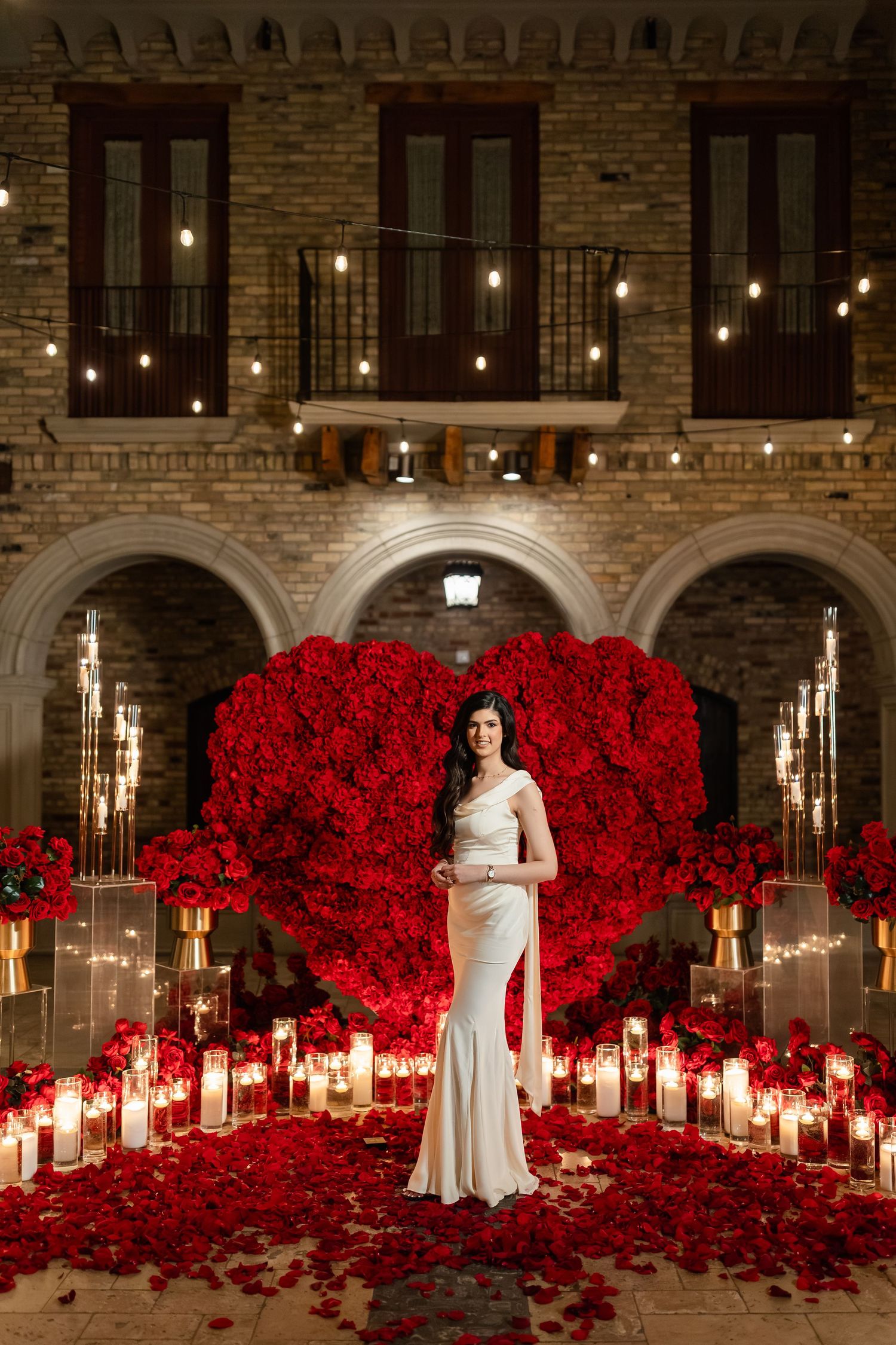 Romantic indoor proposal scene with thousands of red roses and glowing candles in a stone castle-like venue.