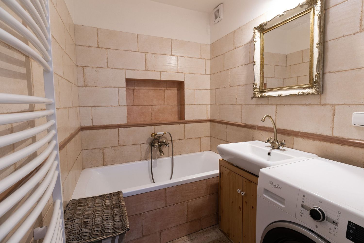 Contemporary bathroom with stone tile walls, bathtub, washing machine and gold-framed mirror.