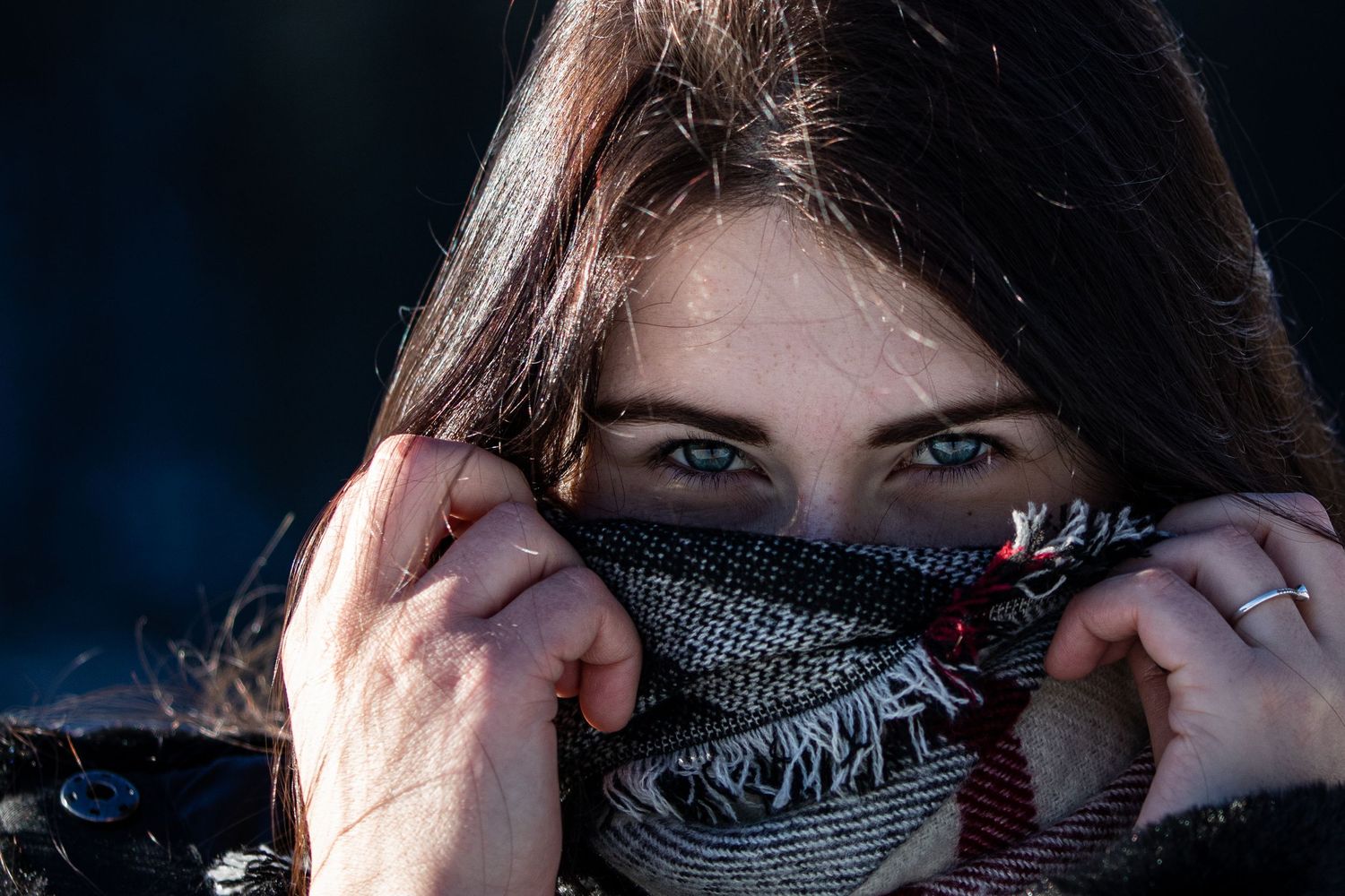 Close up shot of someone pulling up a knit scarf to cover their face in winter.