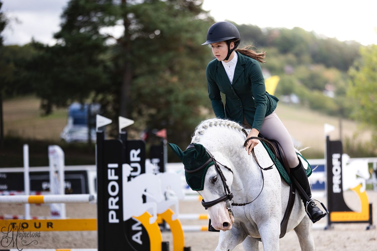 Equestrian rider in dark green show jacket competing in jumping event on white horse at outdoor competition arena.