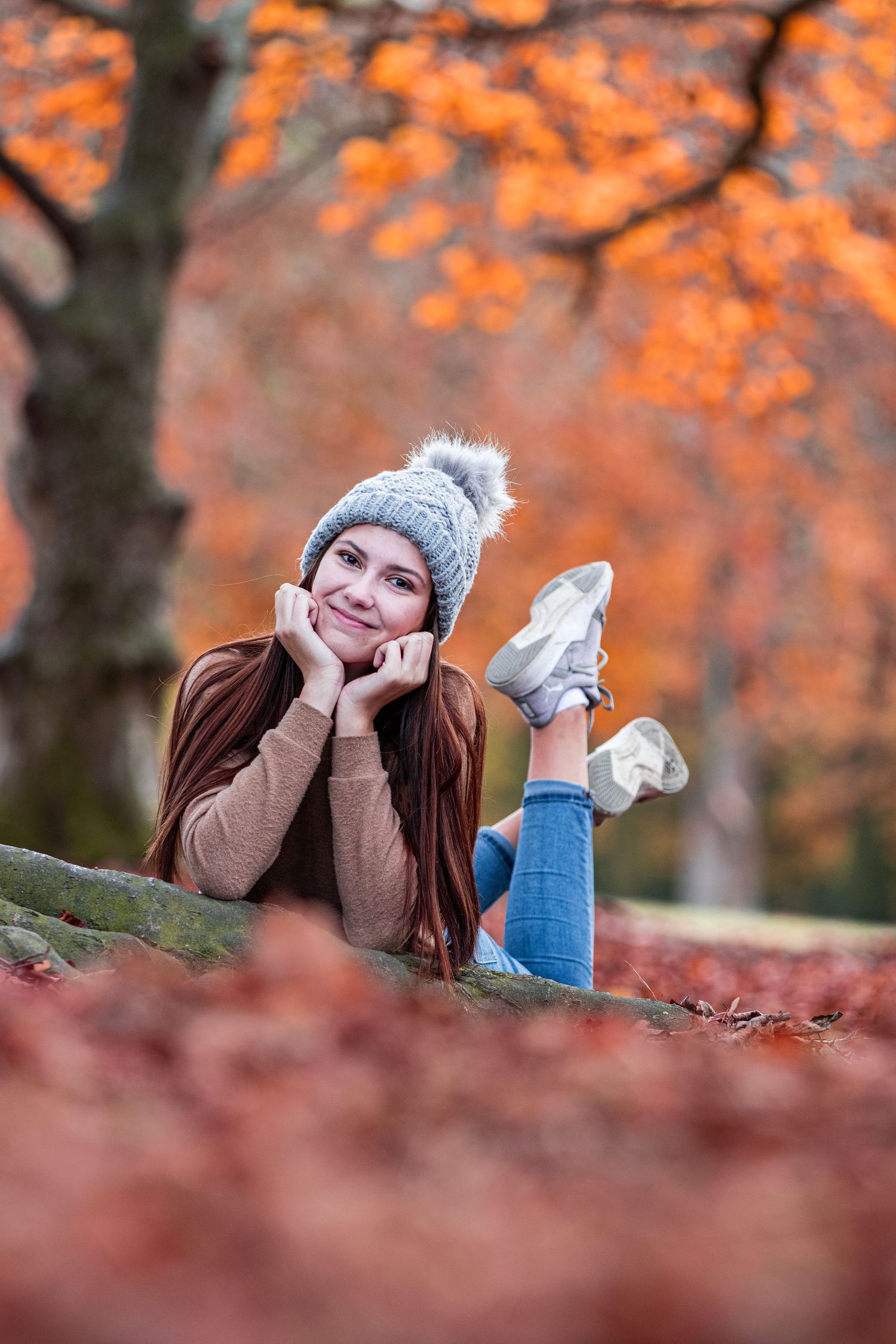 Autumn portrait lying among fallen leaves wearing knit hat with orange foliage background.