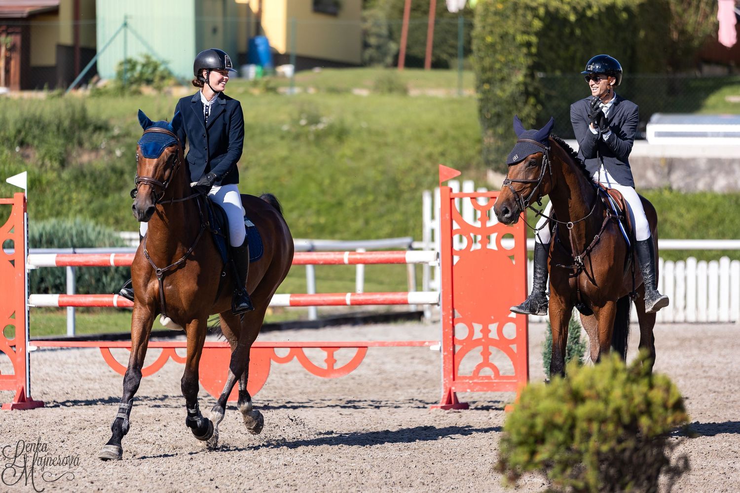 Equestrians riding horses in a show jumping competition at an outdoor arena with red and white barriers.