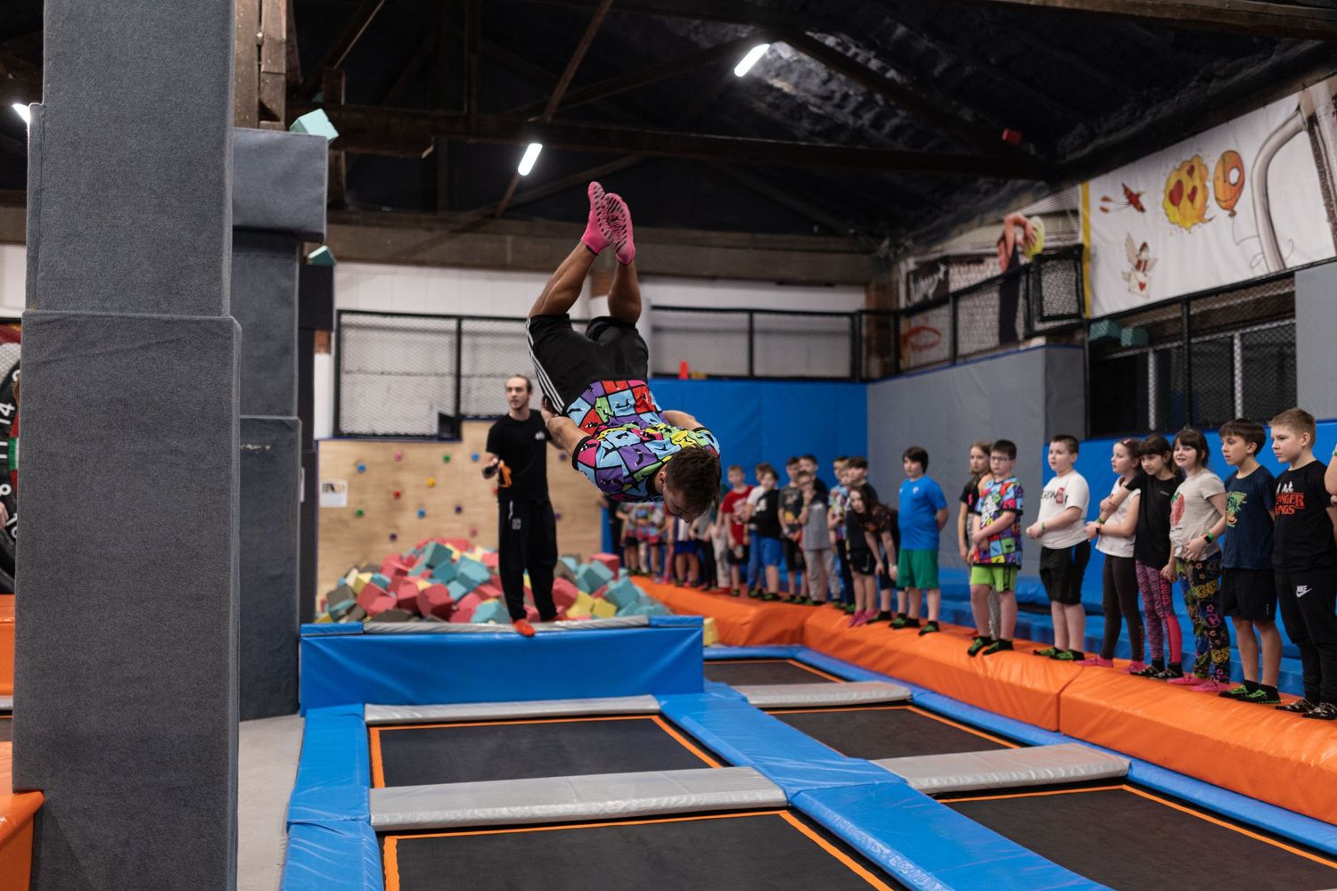 Gymnasts practicing on trampolines in a large indoor training facility with orange and blue safety mats.