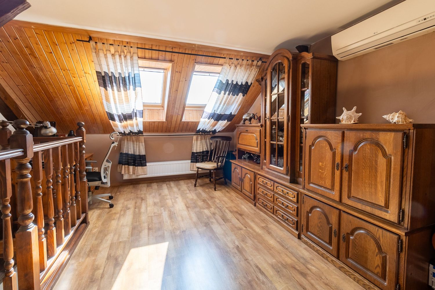 Attic room with wooden ceiling panels, vintage furniture and hardwood flooring.