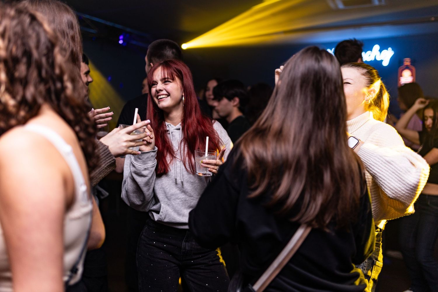 People dancing and socializing at a nightclub with yellow stage lighting in the background.