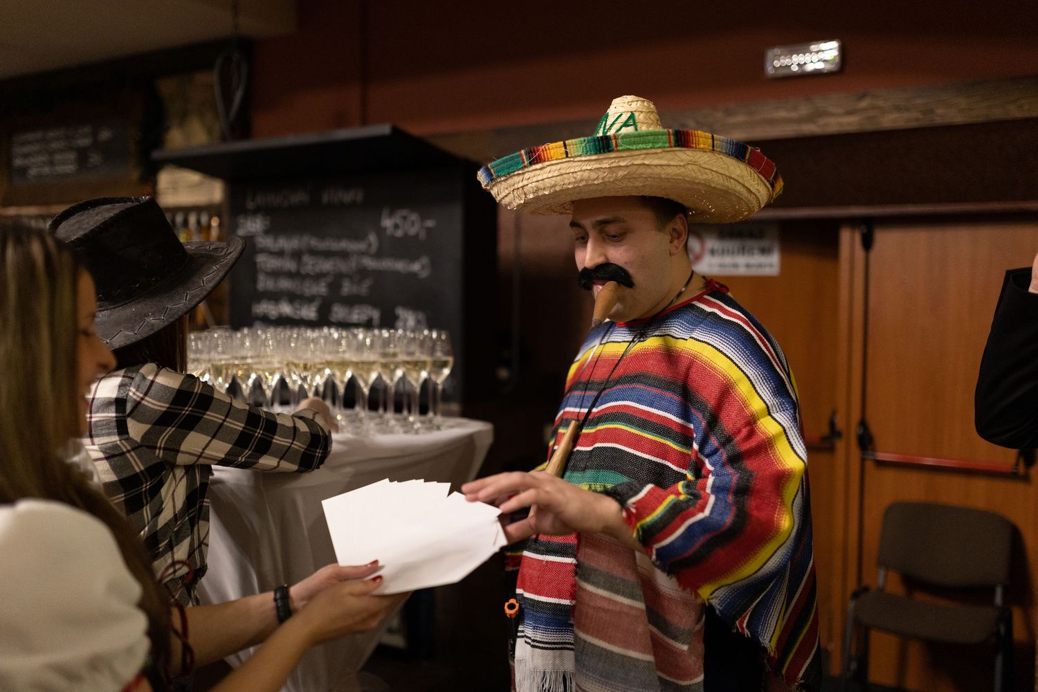 A person wearing a colorful poncho pours a drink into a glass at a rustic wooden bar.
