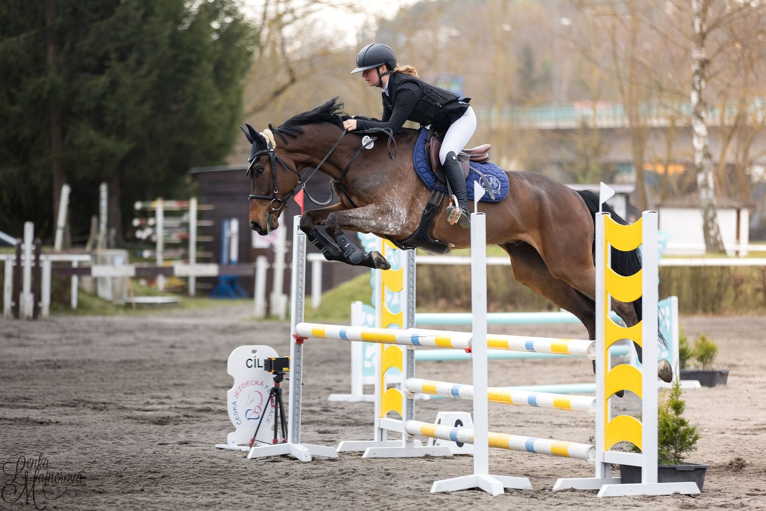 A horse and rider clearing a white and yellow show jumping obstacle during an equestrian competition.