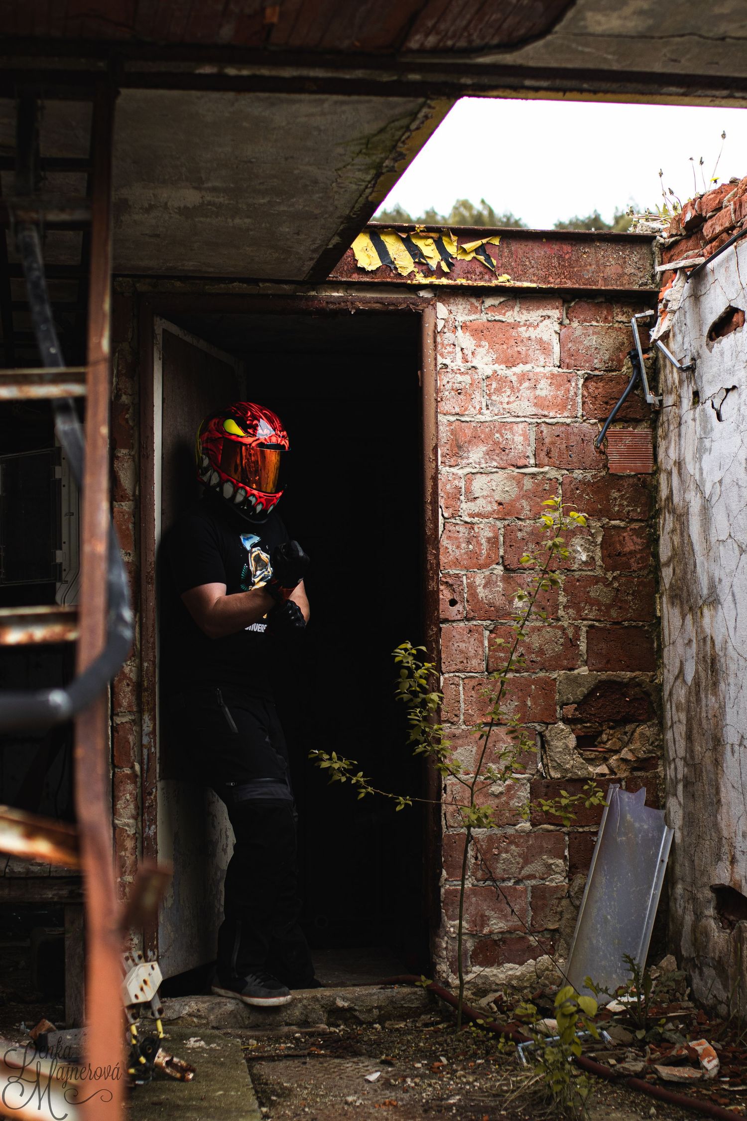 Dark atmospheric photo of figure in red mask standing in doorway of abandoned building.