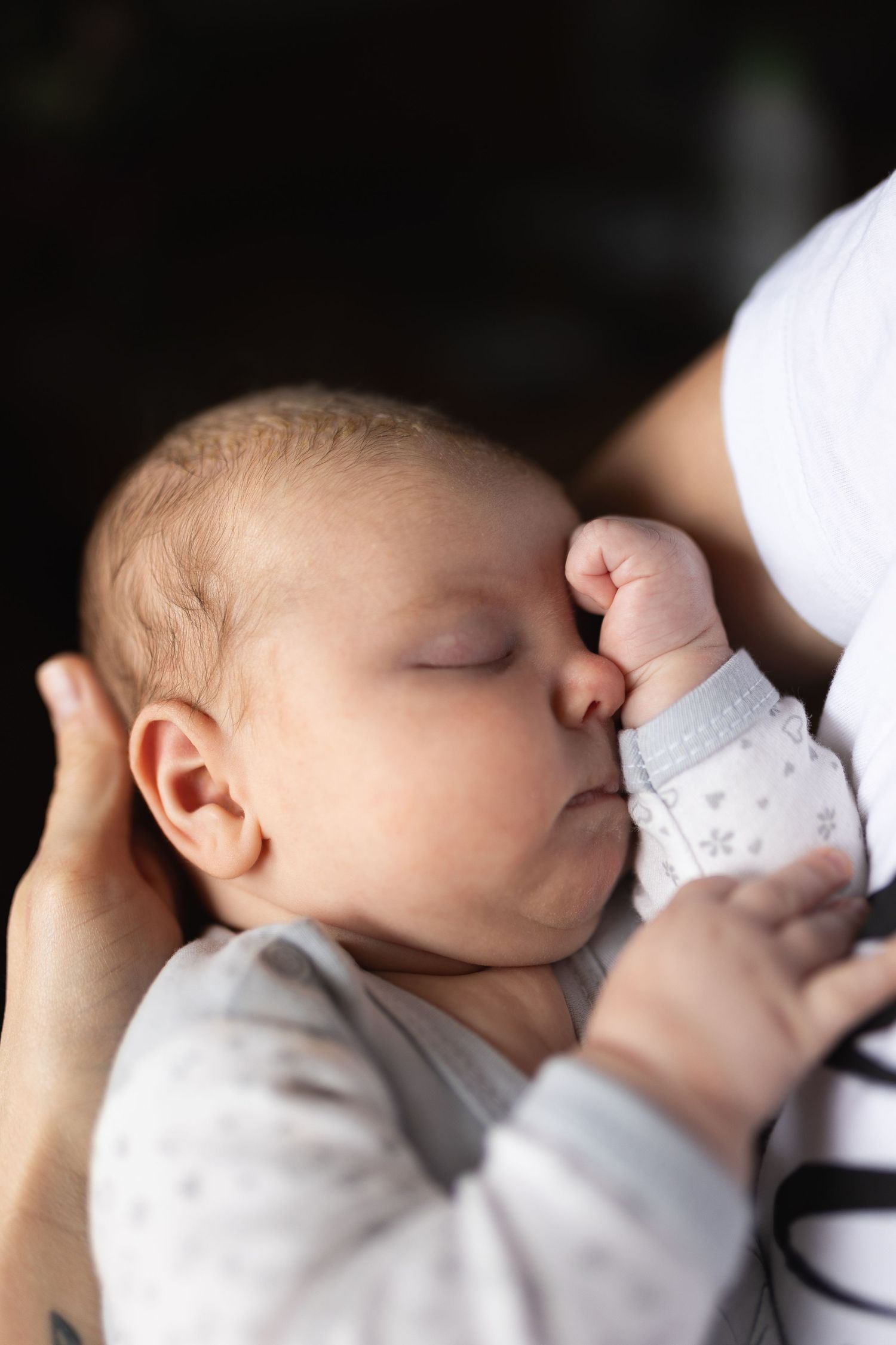 Sleeping baby in white with tiny fist raised near their face.