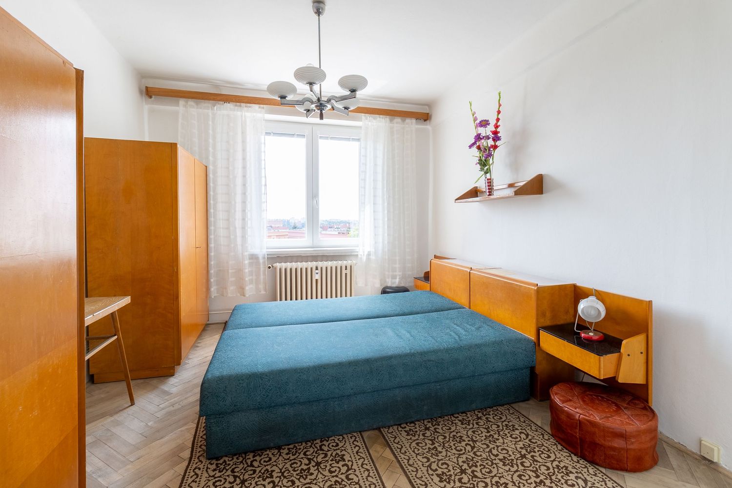 Retro style bedroom with blue bedding, wooden furniture and floral carpet in muted tones.