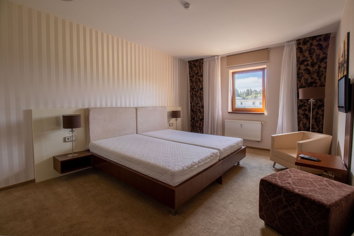 Spacious hotel bedroom with modern furnishings and large window offering mountain views.