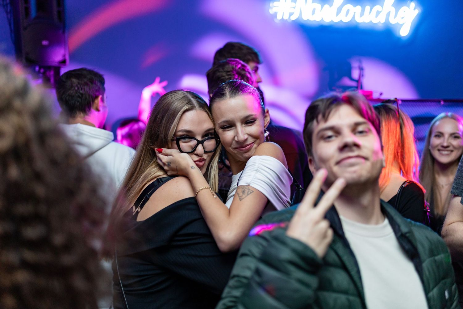 People dancing and embracing in a nightclub with purple lighting and party atmosphere.