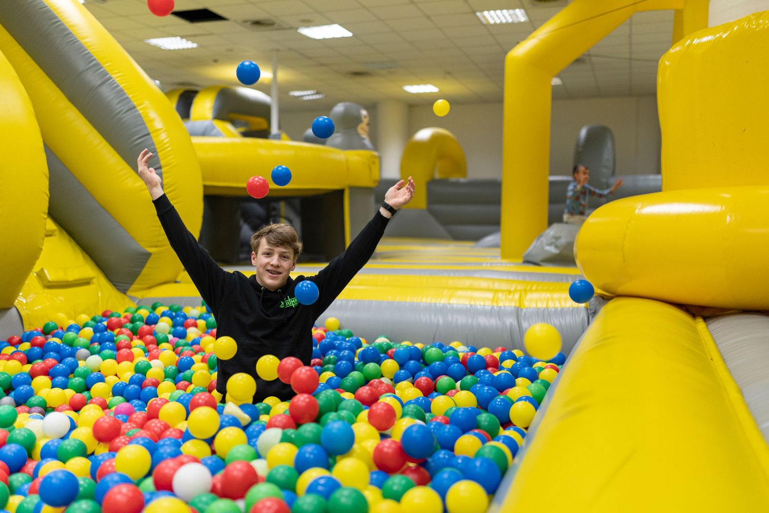 Children playing in a colorful indoor inflatable playground with yellow bouncy structures and ball pit filled with multicolored balls.