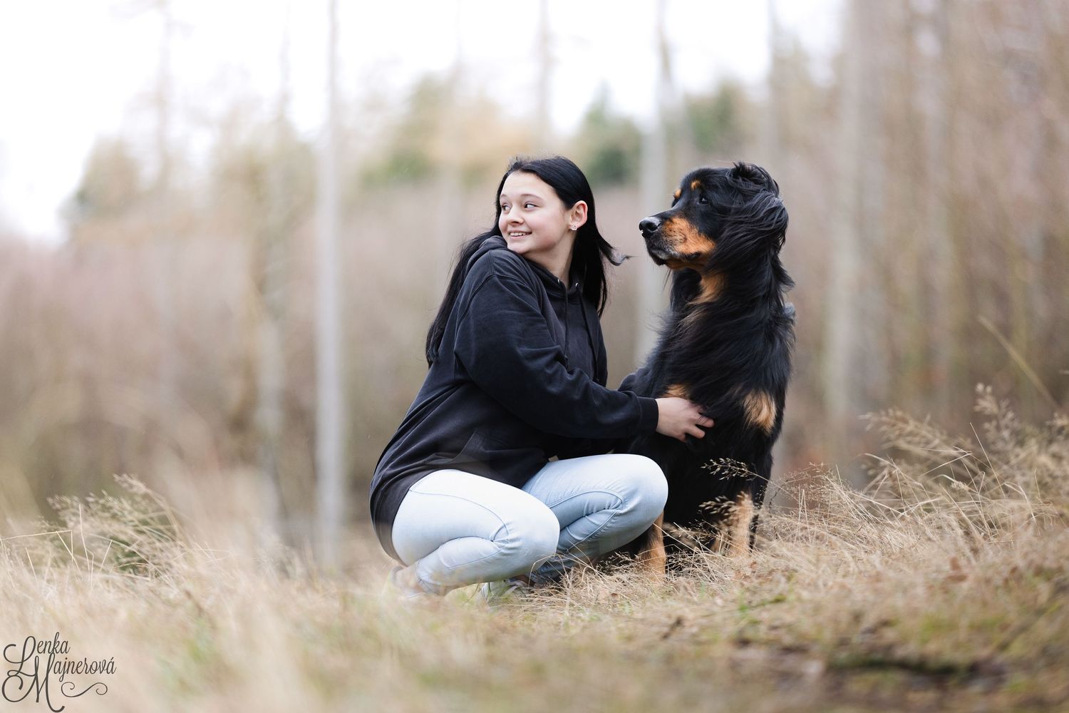 A person sits in a grassy field with a black dog during a serene outdoor photo session.