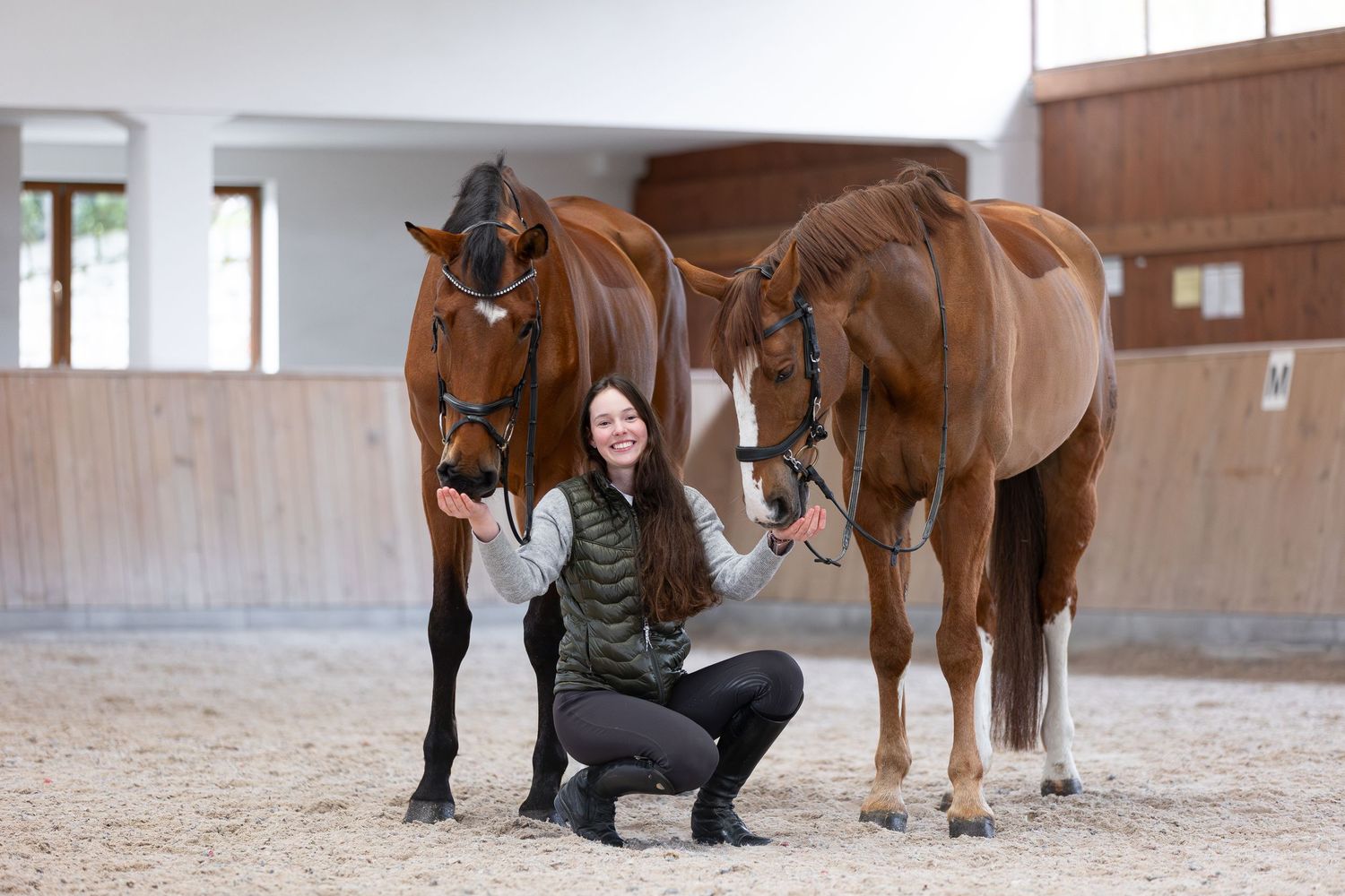 Two brown horses standing with someone in a riding arena.