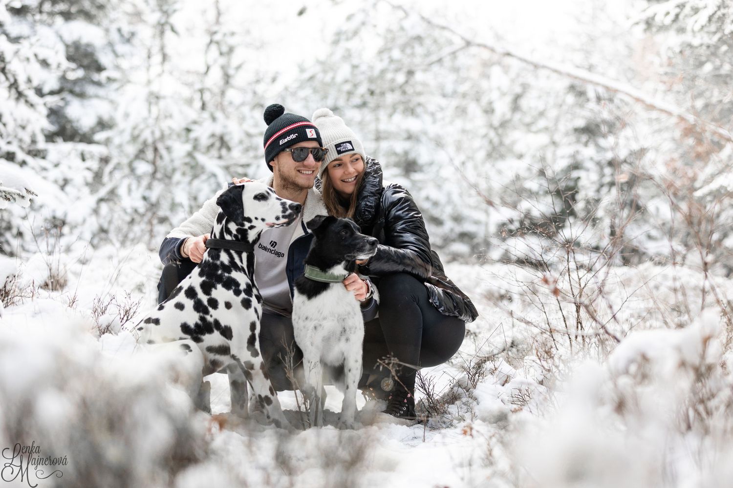 Dogs and companions posing together in snowy winter forest setting.
