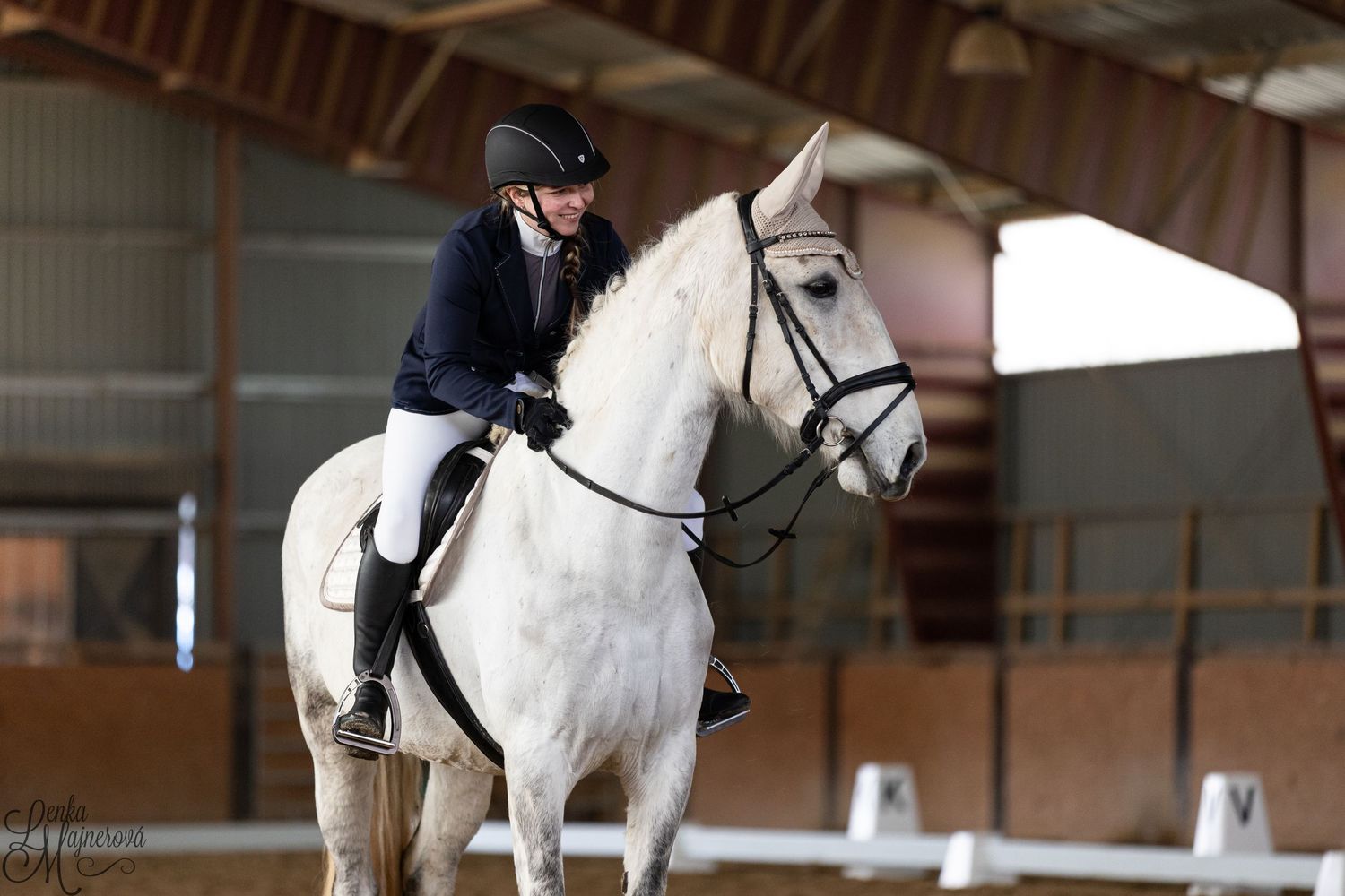 Rider on white horse practicing dressage in indoor riding arena.