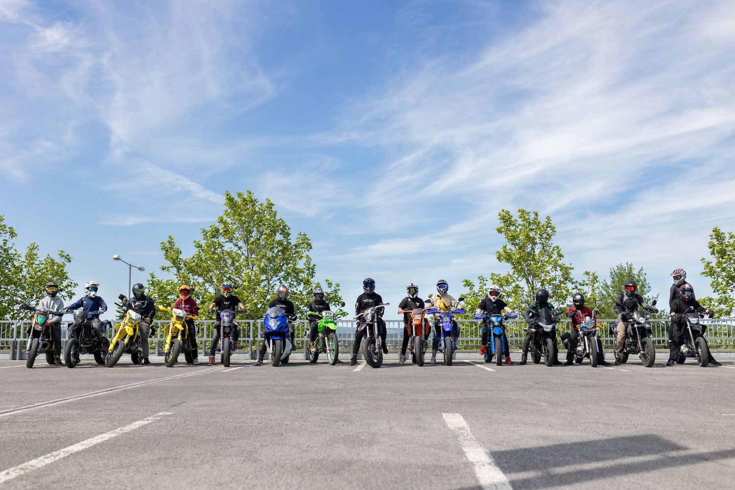 A long line of motorcyclists wait in formation on a sunny day during an outdoor motorcycle event.