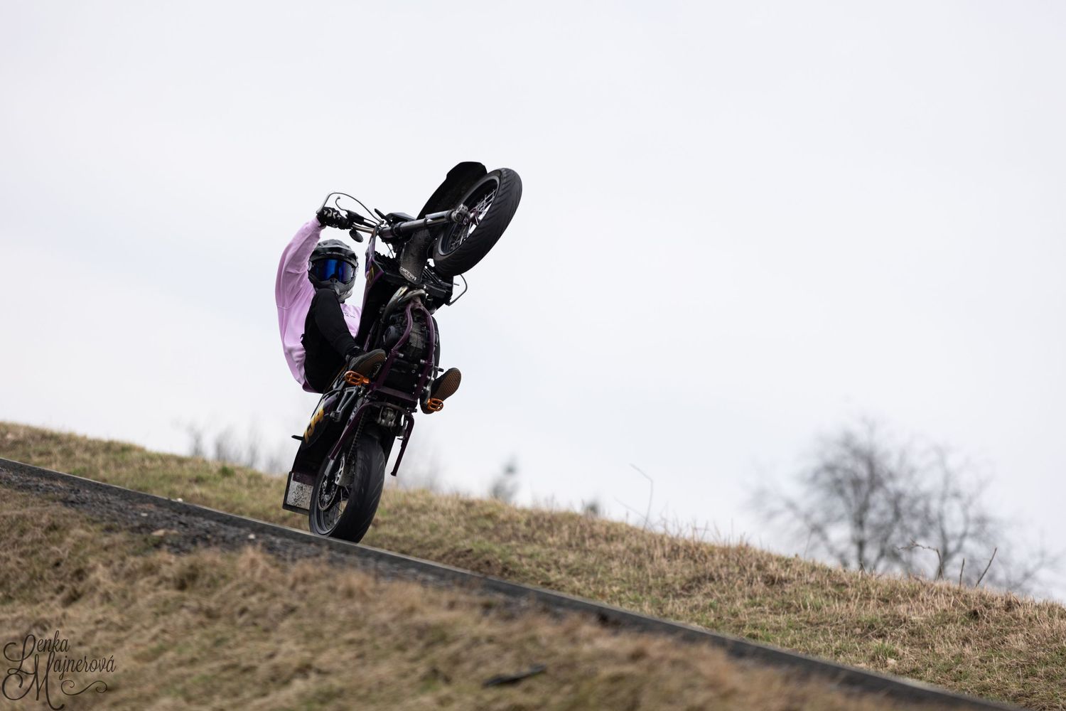 Dirt bike rider executing wheelie on hillside terrain.