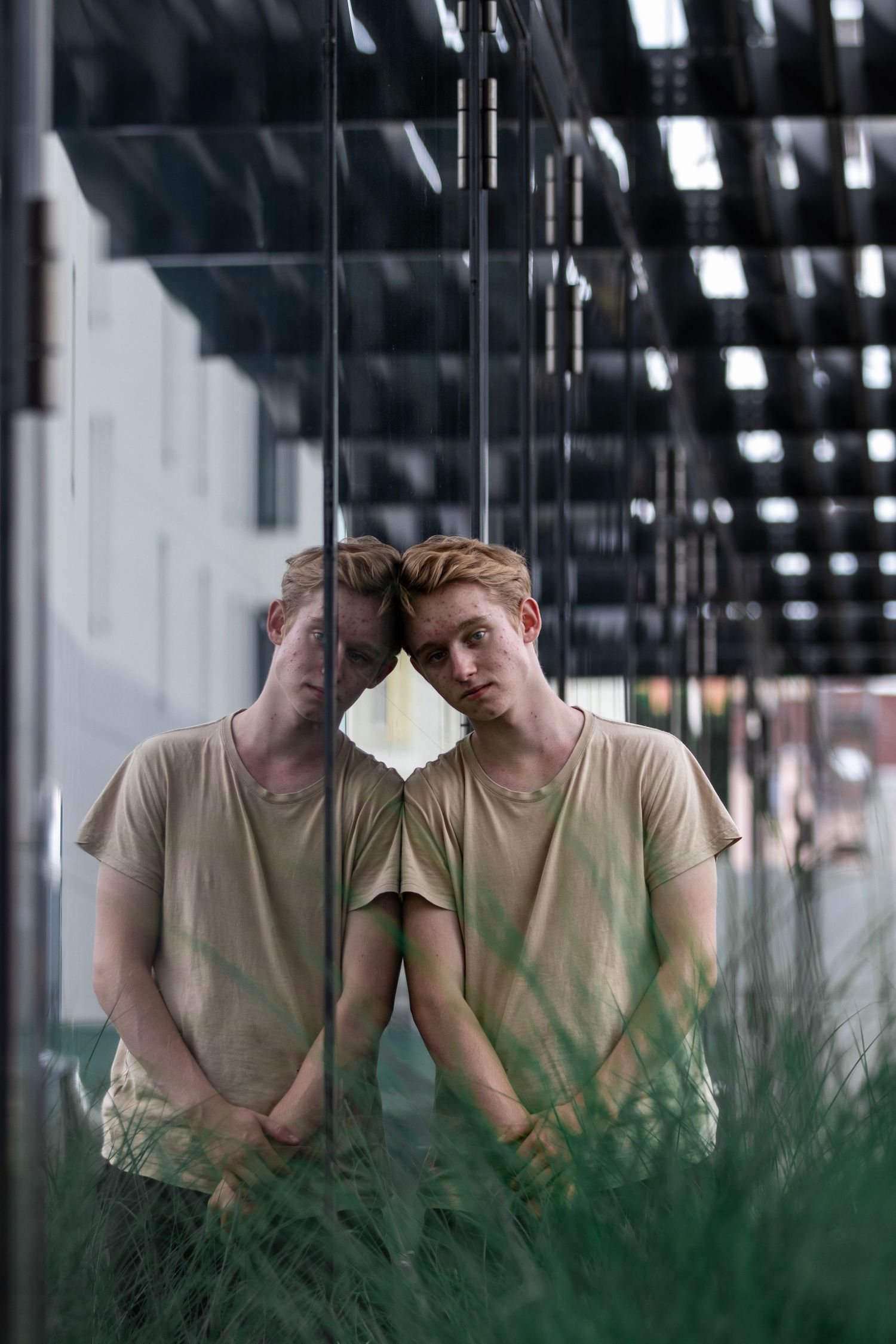 Creative mirror reflection portrait through glass with plants in foreground.