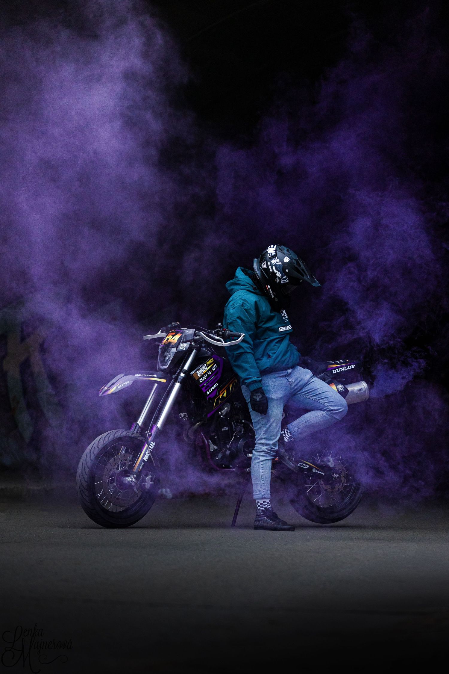 Motorcycle stunt sequence with purple smoke showing rider crouching low against dark background.