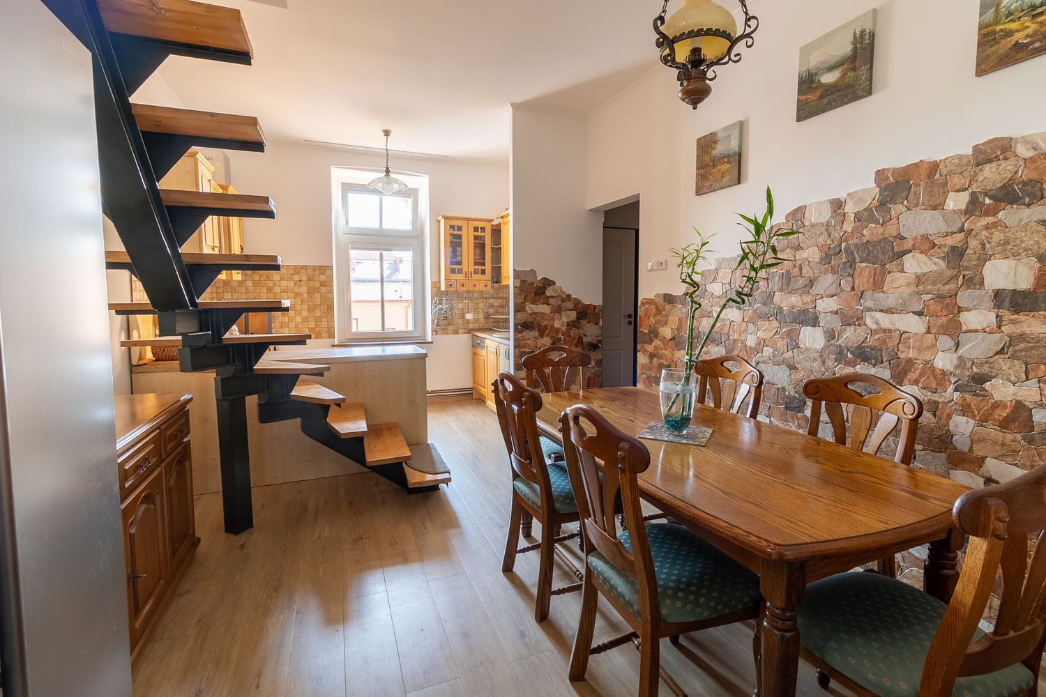 Modern dining area with floating staircase, wooden table and stone accent wall.