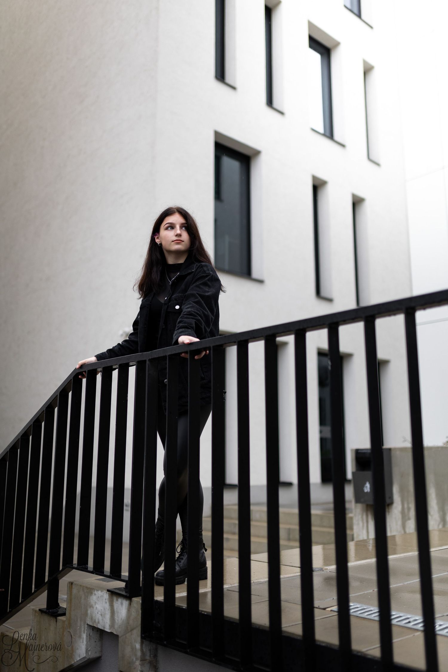 Fashion portrait on black metal staircase against white modern architecture.