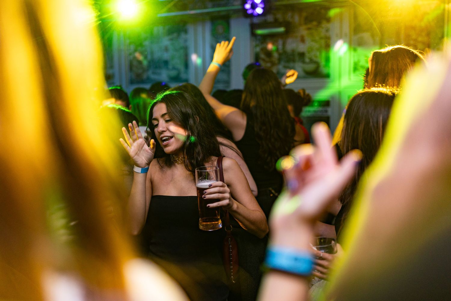 Colorful nightclub scene with people dancing and partying under vibrant green and yellow lighting effects.