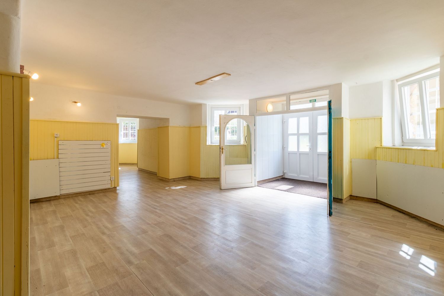 Empty classroom or activity room with yellow walls and wood flooring featuring natural lighting from multiple windows.