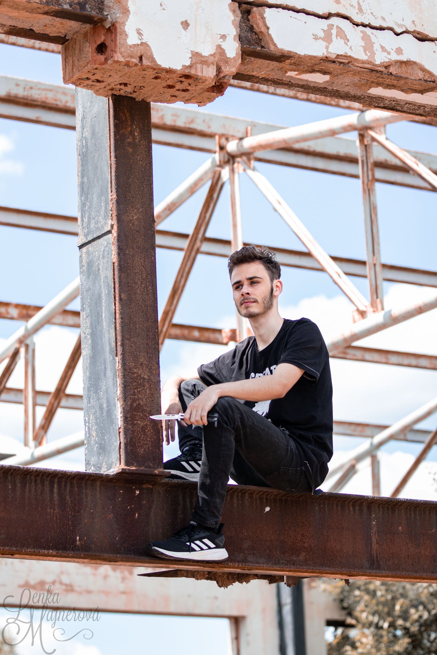 Person sitting on rustic metal beam structure against blue sky.