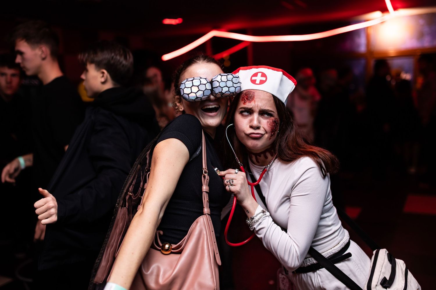 Crowded dance floor at a nightclub with red lighting and people dancing in a dimly lit environment.