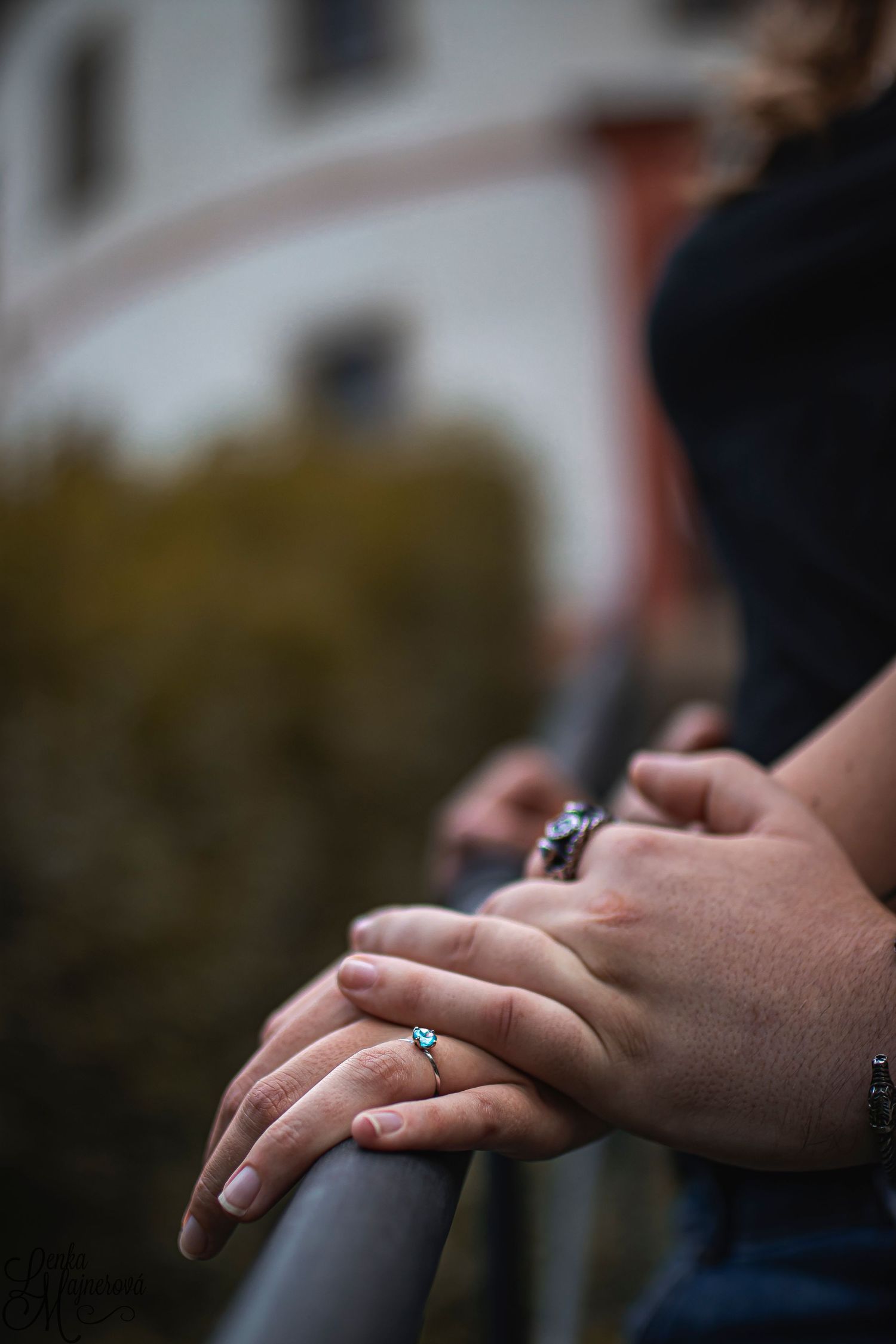 Close-up of hands with rings resting on metal railing with blurred background.