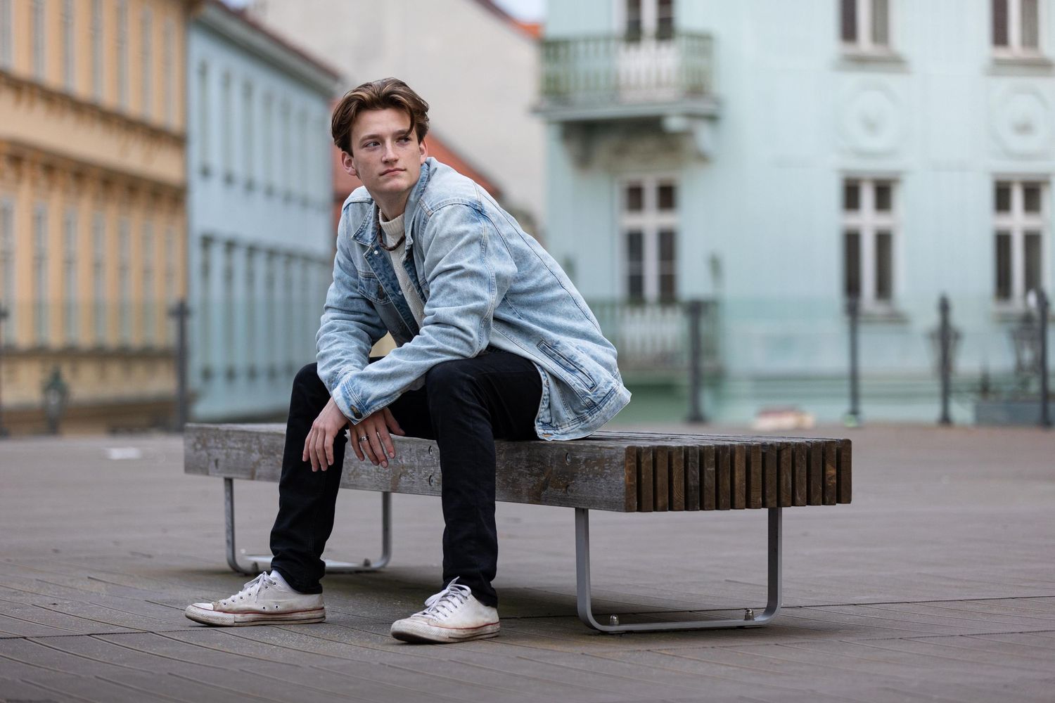 Casual street style portrait on modern bench against pastel colored buildings in urban setting.