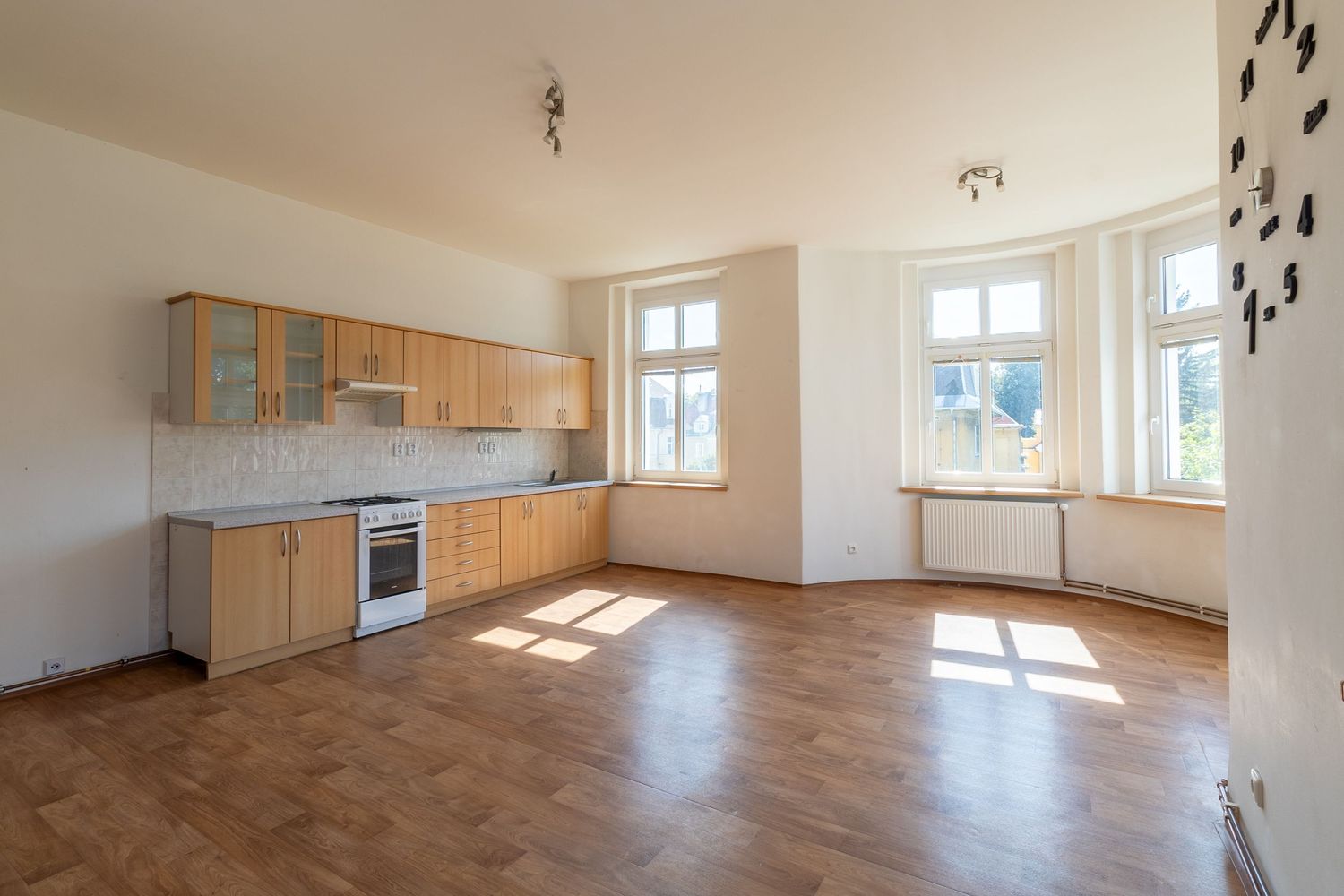 Empty apartment kitchen with wooden cabinets, white walls and parquet flooring.