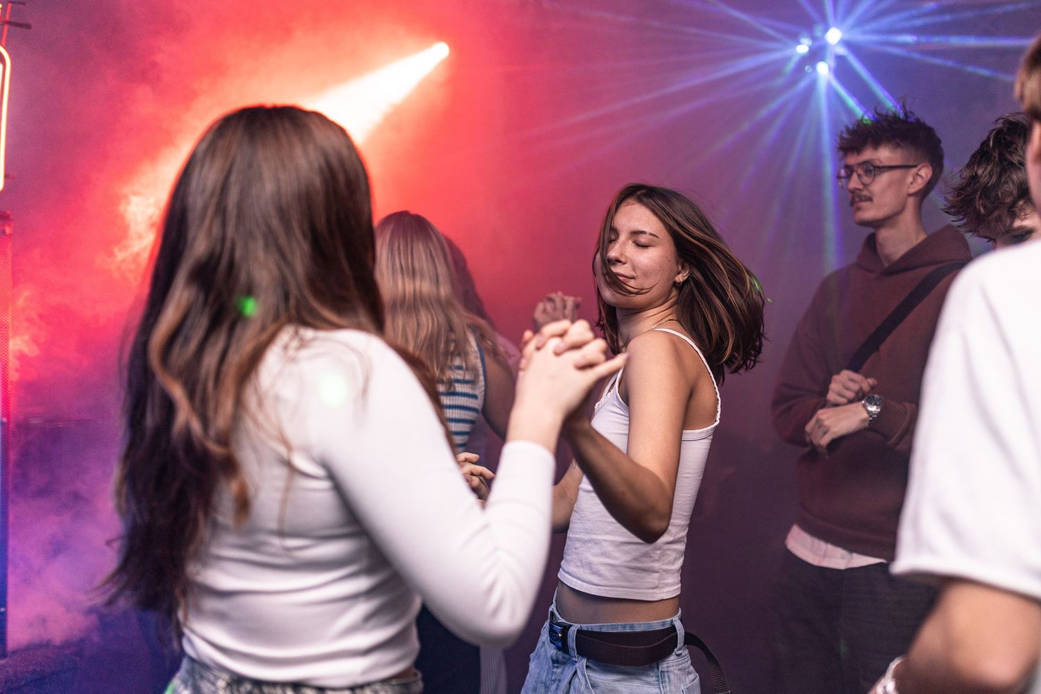 People dancing and having fun at a nightclub with colorful red and blue lighting effects in the background.