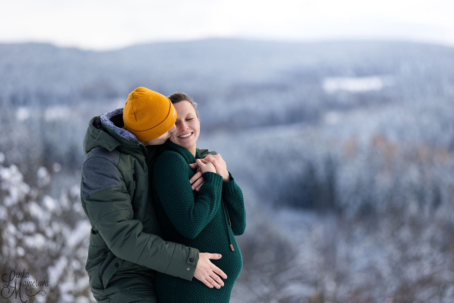 Couple embracing in winter clothing against a snowy mountain backdrop.
