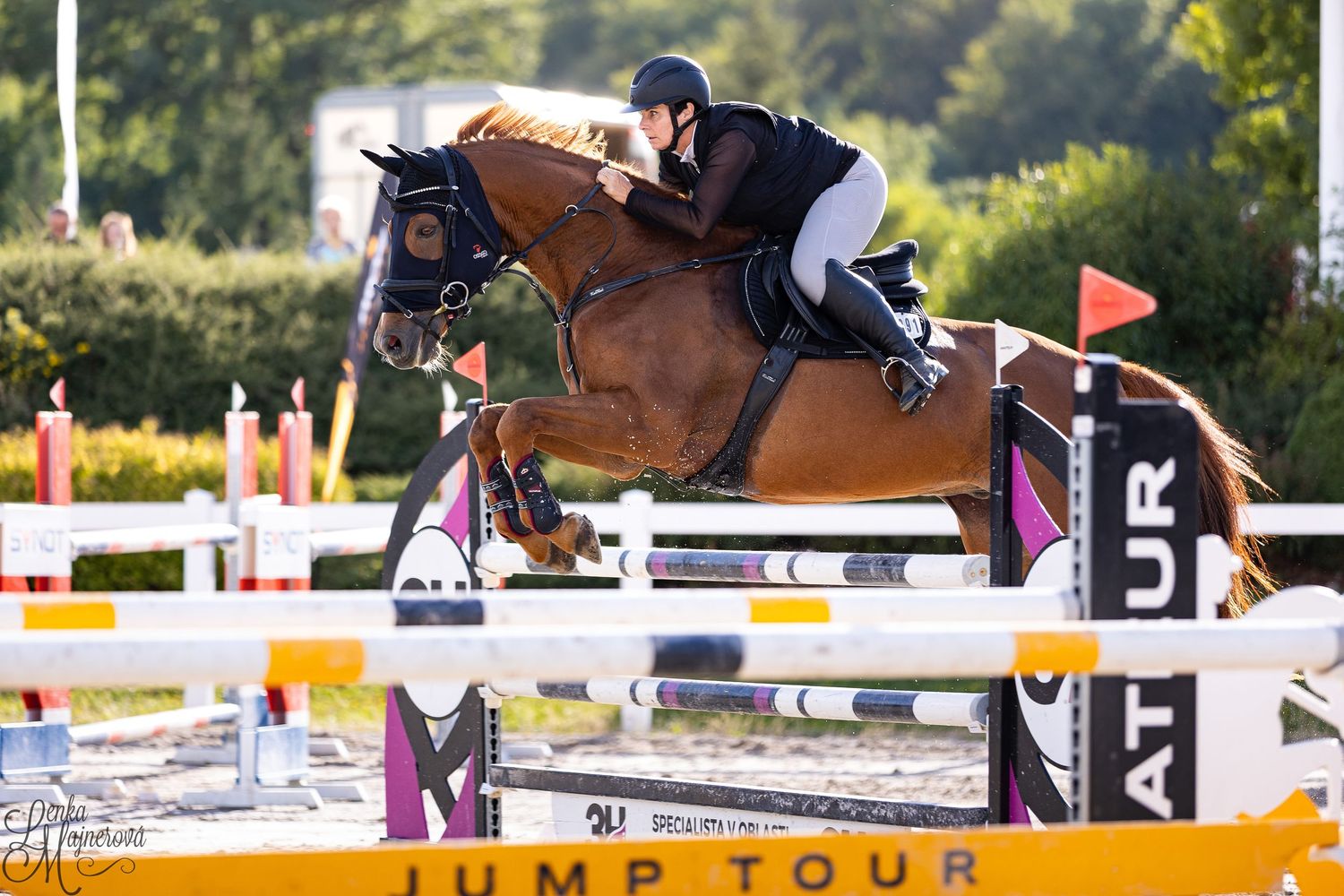 A rider on horseback clearing a jump during an equestrian competition on a sunny outdoor course.