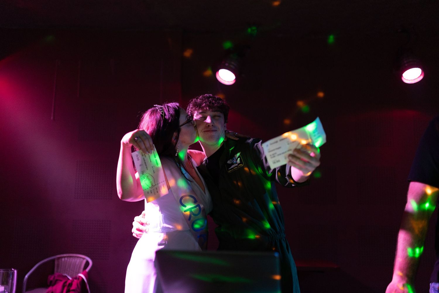Colorful lights illuminate a dark concert venue with silhouettes of performers and equipment on stage.