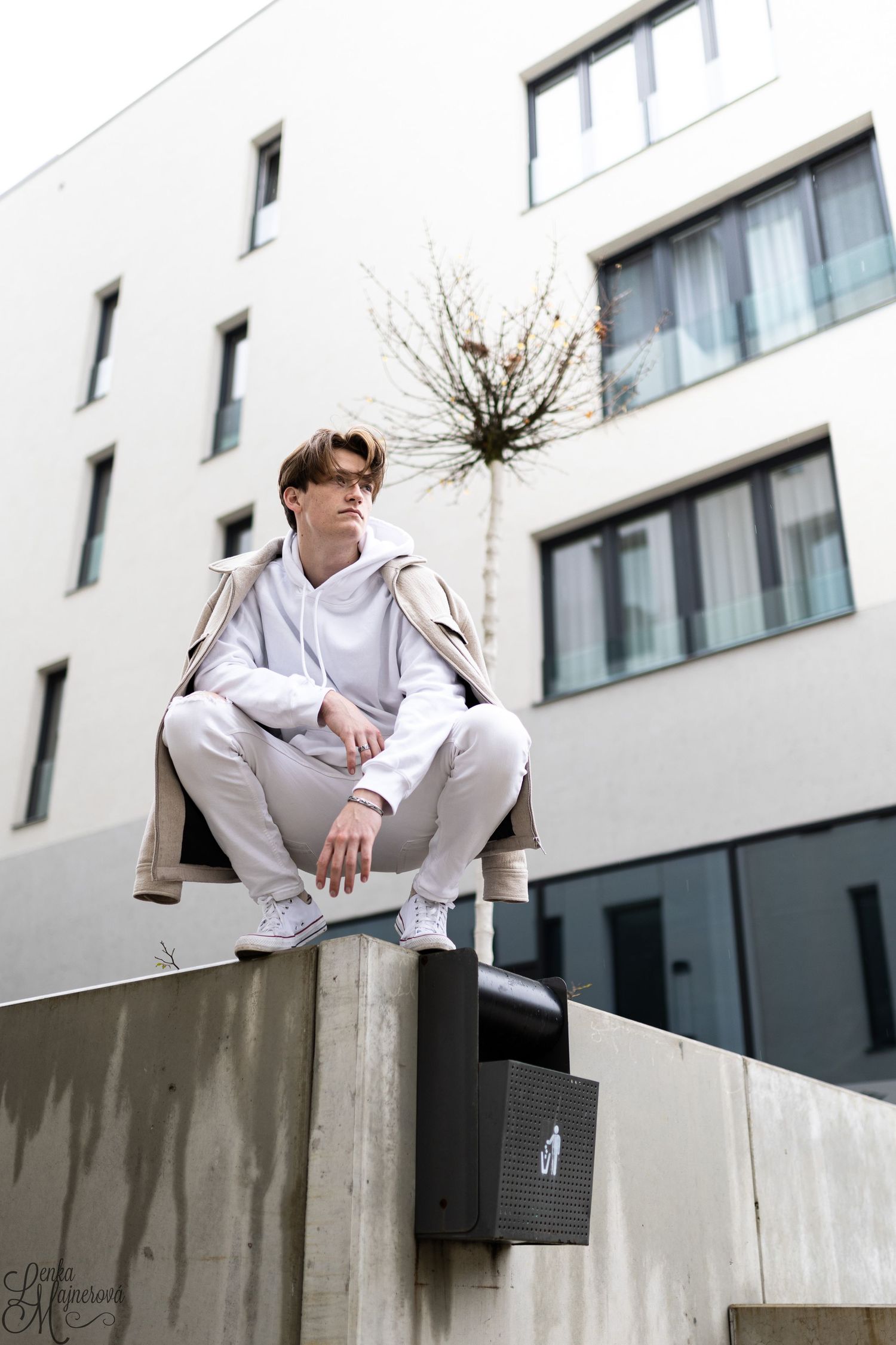 Person in white outfit sitting on concrete wall near modern building.