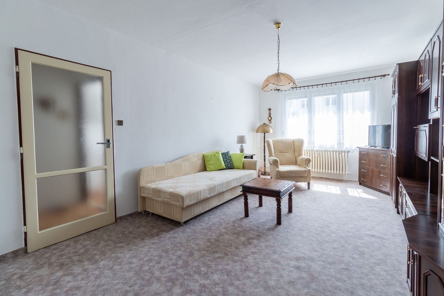 Minimalist living room with beige sofa, carpeted floor and large window with sheer curtains.