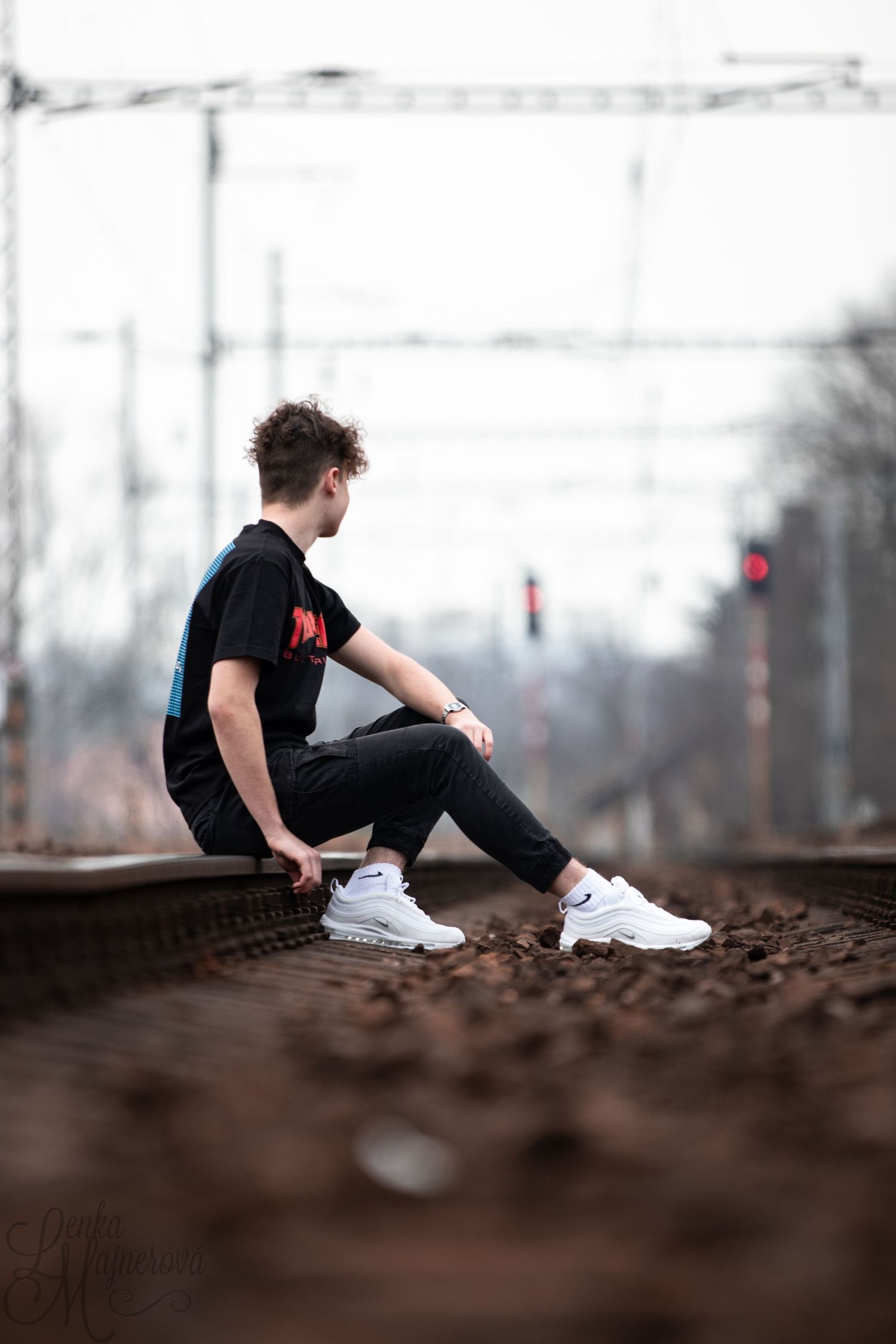 Person in black outfit sitting on train tracks wearing white sneakers.