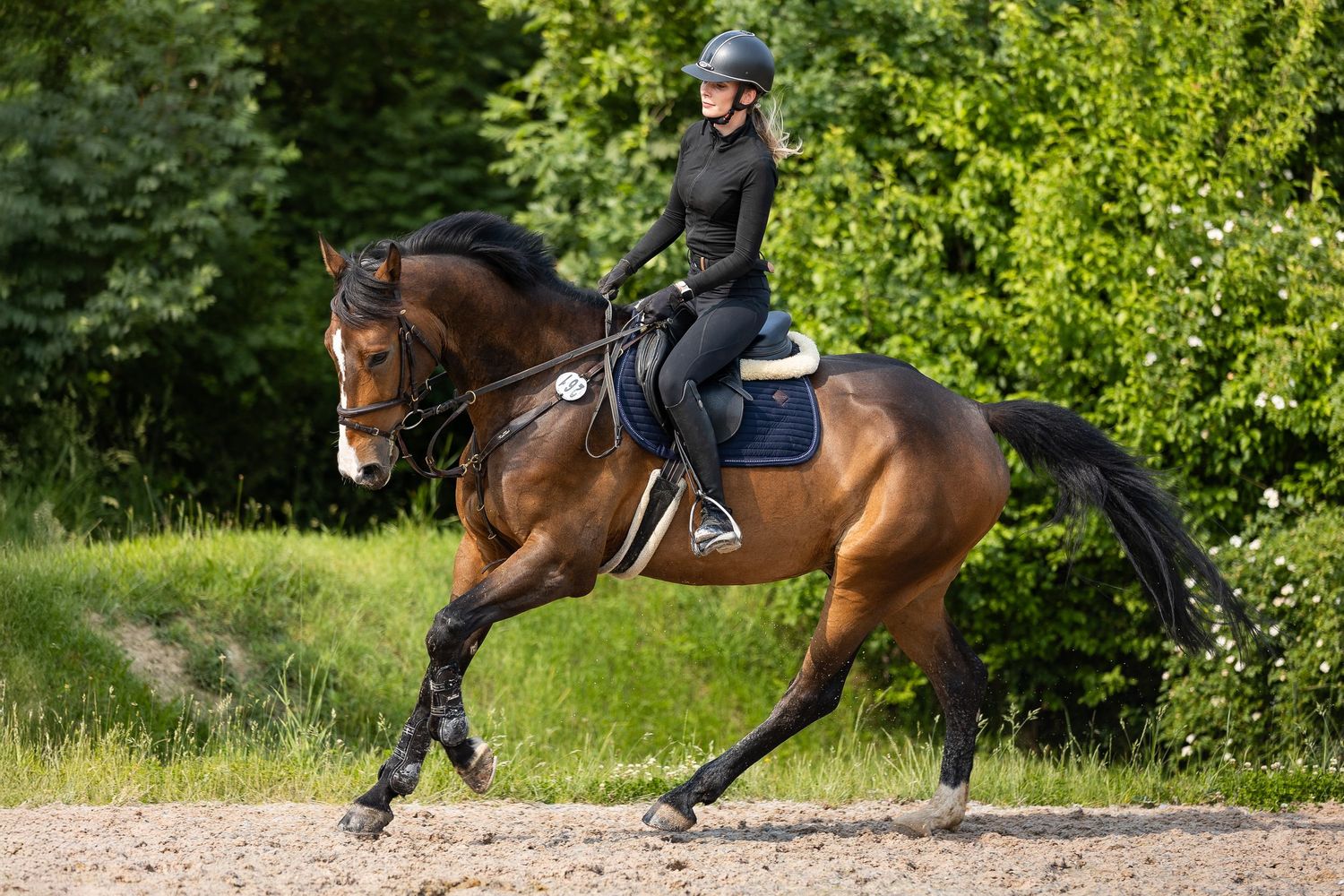Close-up view of horse hooves and riding boots galloping on a dirt path through lush green foliage.