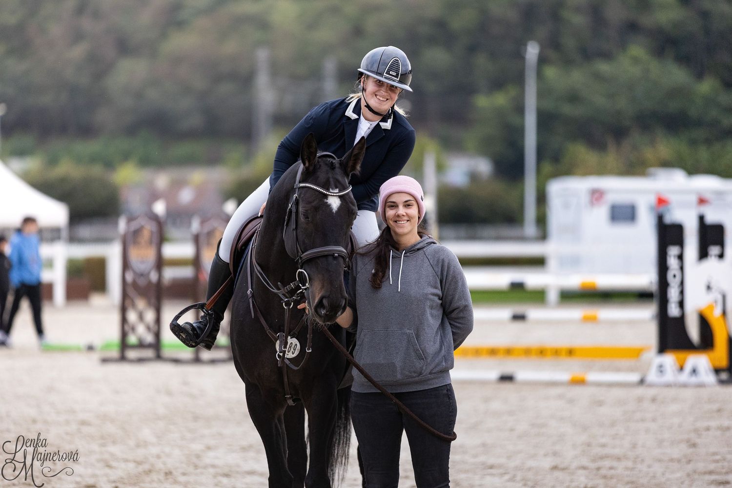 A person leads a black horse through an outdoor equestrian arena during a training session.